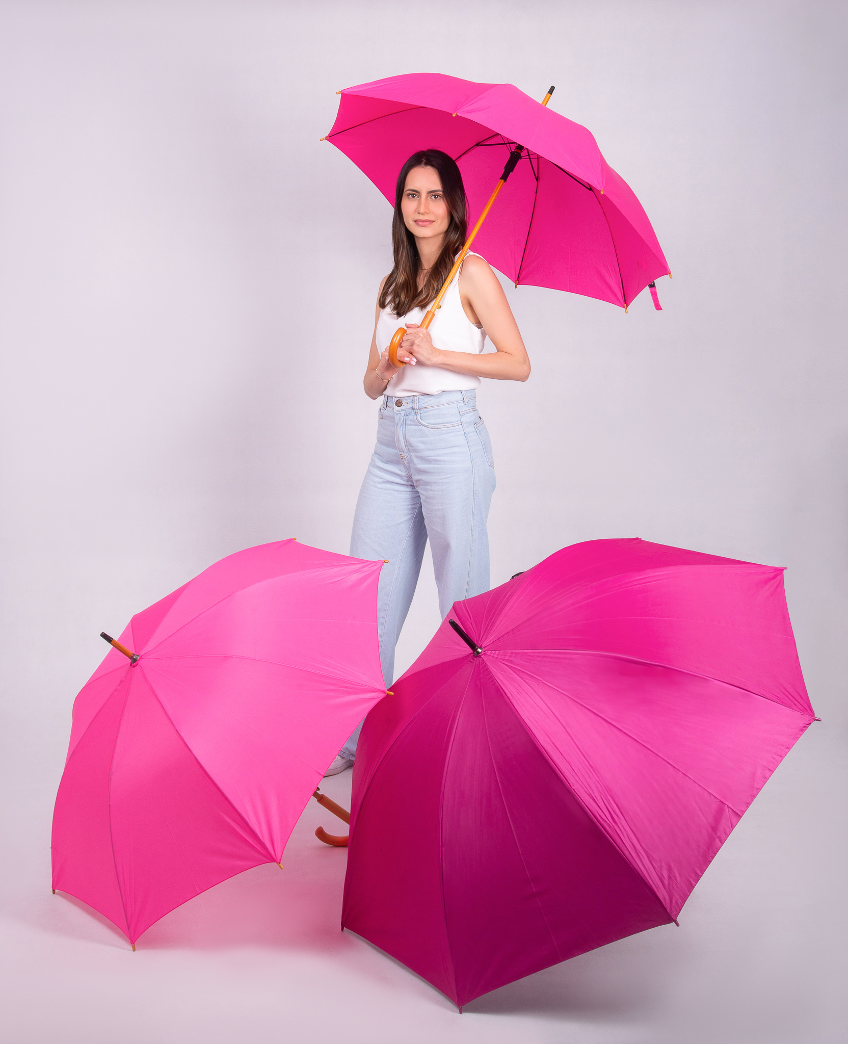 Mulher segurando guarda-chuva rosa da Florença, com guarda-chuvas rosa e pink abertos, brinde para campanha Outubro Rosa